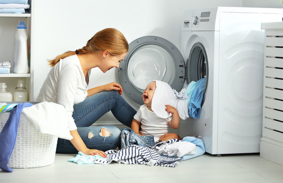 Mother A Housewife With A Baby  Fold Clothes Into The Washing Ma