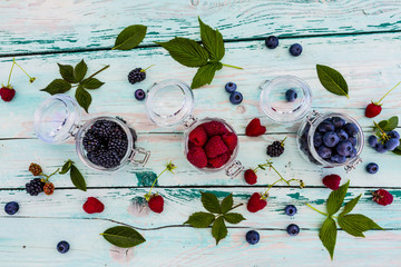 Tasty and fresh forest berries in jars on wooden table.