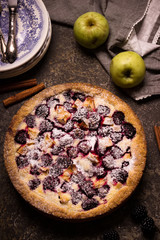 Homemade pie with apples and blackberry on dark stone background.