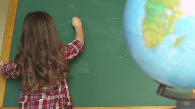 young girl writing the numbers on chalkboard