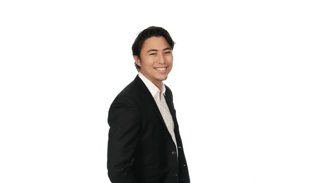 Video shot in 4k of an attractive businessman in a black suit and white shirt, standing against a white background smiling against camera.