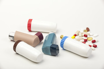 Various types of asthma inhalers and some pills on white