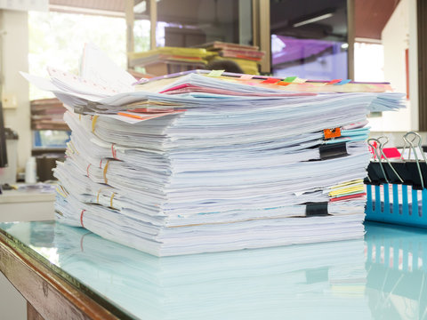 Pile of unfinished documents on office desk with businessman background