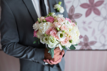 groom holding a wedding bouquet of white roses