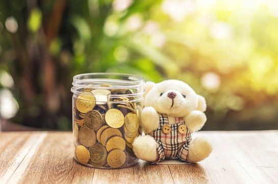 money (coins) in the glass with teddy bear Investment and Interest Concept. Filter soft effect and warm sunset.