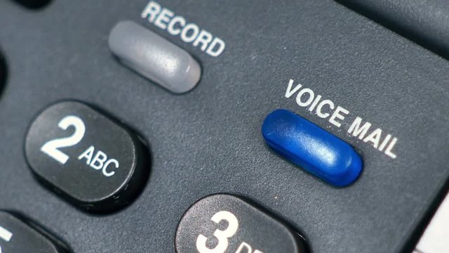 The blue blinking telephone message light on a desk phone indicating there is voice mail.
