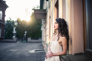Beautiful girl on white dress walking on a warm sunny day in the city. Young brunette long-haired beautiful woman, lifestyle concept