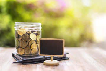Money (coins) in the glass with noted book, copy space frame, Investment and Interest Concept. Filter soft effect and warm sunset selective focus.