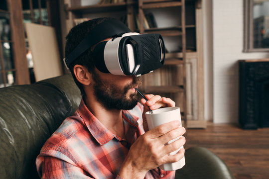 Man Drinking Cocktail While Using Vr Glasses At Home. Guy Enjoying Movie In Virtual Reality Headset And His Smoothie In Ceramic Glass Close-up. Cinema At Home, Innovation, Entertainment Concept