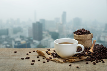 Hot Coffee cup with Coffee beans on the wooden table and the cit