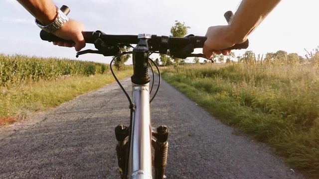 Riding on a MRB bike in summer evening countryside on dirty road, view to handlebars and landscape with sunligh. Bike riding concept, healthy cyclo exercise in the fresh air, outdoor sport activity