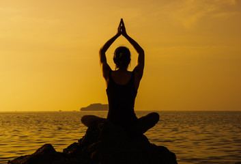 Yoga woman sitting in lotus pose on the beach during sunset