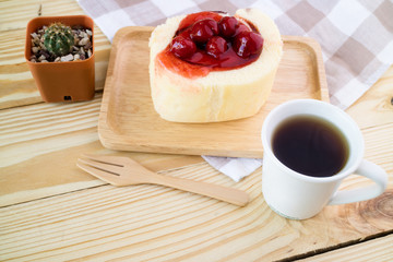 Hot espresso coffee with strawberry cake roll on wood table.
