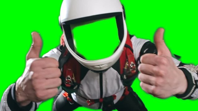 Excited skydiver in full parachuting gear, white helmet, jumpsuit and harness, showing both thumbs up and looking at camera, no face chroma key template for video editing,green screen background