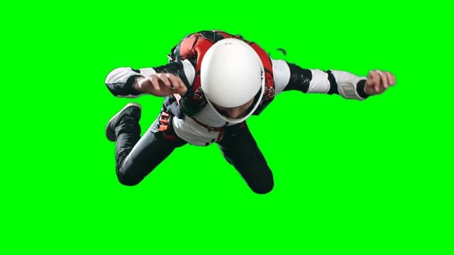 Front view Locked down slow motion shot of skydiving man performing free fall in full parachuting gear, jumpsuit, helmet and harness, against green background, extreme sports chroma key