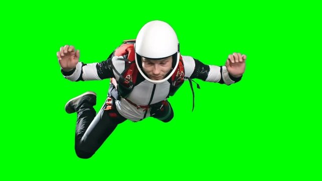 Slow motion shot of professional skydiver turning in free fall, man in full parachuting gear helmet, jumpsuit and harness, chroma key against green screen background