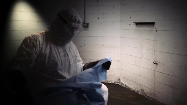 doctor in hazmat gear puts a sheet over someone on the floor