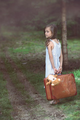Young girl barefoot in the woods with a suitcase