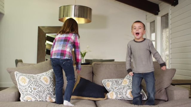 Slow motion brother and sister jumping on the sofa in the living room