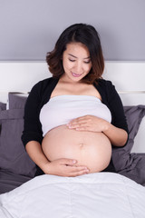 pregnant woman looking at her belly while lying on bed