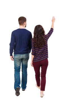 Back view of walking young couple (man and woman) pointing. Swarthy girl and the bearded man walk away seeing something in the sky.