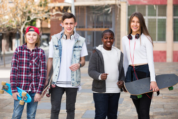 Four teens with skateboards outdoors.