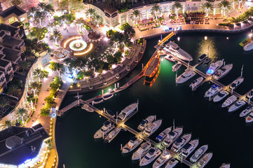Fototapeta premium Amazing colorful dubai marina fountain and yacht dock during night. Beautiful sidewalk among tallest skyscrapers of the world. Dubai marina, United Arab Emirates.