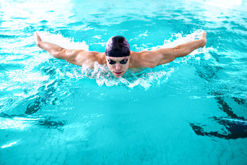 Fototapeta na wymiar Portrait of strong professional swimmer in black cap and goggles in pool.Butterfly style.