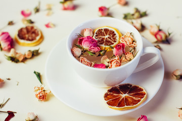 Herbal tea in white Cup and saucer with roses and dried flowers dried round slices of lemon laid on a white background