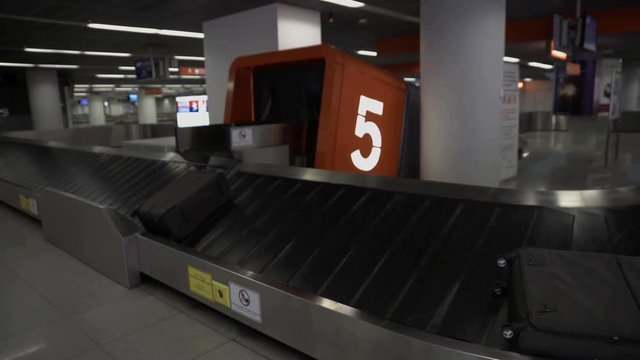 There is a luggage on a carousel and the carousel is moving. There are only a few black suitcases left. Wide-angle shot.
