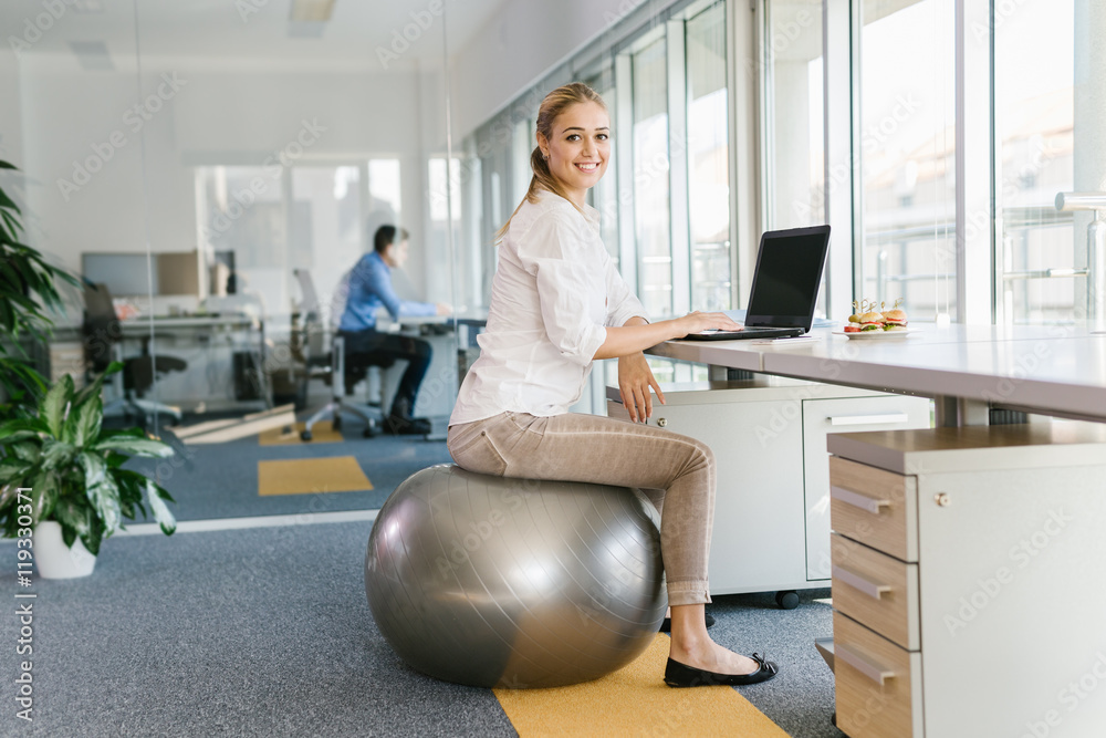 Wall mural business woman working on laptop in office while sitting on pilates ball