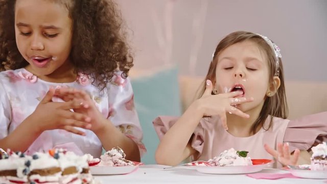 Adorable little princesses eating birthday cake at the table and licking fingers in slow motion