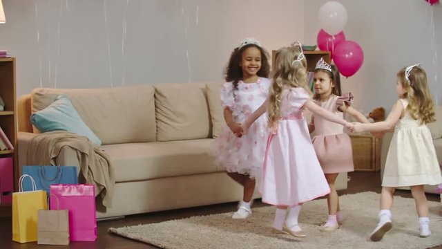 Four Pretty Girls Dressed Like Princesses Dancing In Circle And Changing Direction In Decorated Children Room At Birthday Celebration