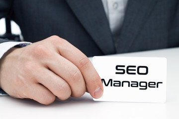 SEO manager sitting at the desk and shows his business card.