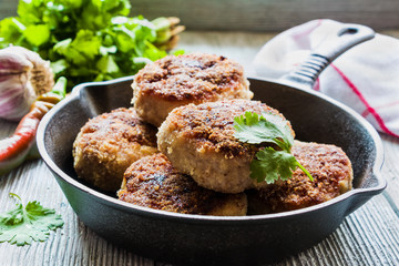 Chicken  roasted cutlets in black cast-iron skillet, fresh vegetables and parsley on wooden...