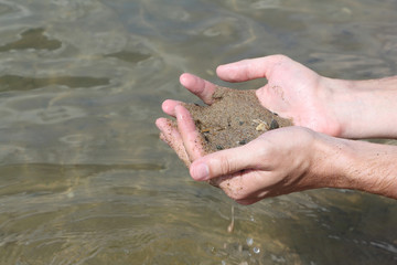 Male palms with damp river sand against a surface of the water