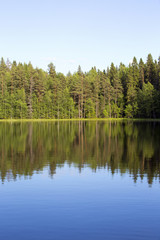 Obraz premium Silent evening by the lake. The sun is about to go down in Finland during late summer evening. The water is reflecting nicely the forest in the background.