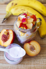 Vertical photo of fruit salad mixed with fresh yogurt, banana, plum and nectarine on wooden background
