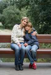 happy mother and daughter sitting embraced on bench