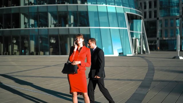 Young pretty sexy businesswoman in red dress talking smartphone. Businessman in suit and tie shy to contact with female outdoor in business glass building district. 4k ultra hd. wide shooting.
