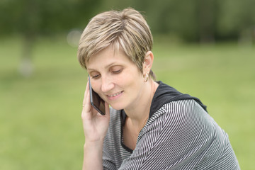 young woman with short hair talking on phone in the Park