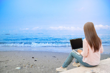 Young beautiful woman working outdoor on the beach at the sea. Working on laptop outdoors. Cropped image of female working on laptop while sitting at the sea.