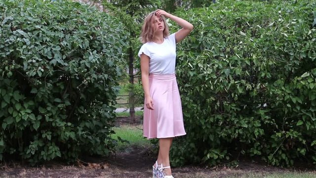 Young girl in pink skirt straightens hairstyle next to large shrubs