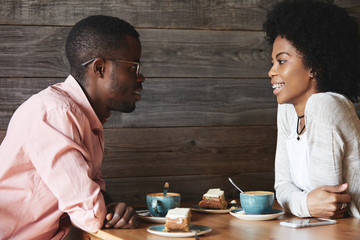 Happy dark-skinned couple having nice conversation after long breakup, looking at each other with amorous eyes against wooden wall with copy space for your advertising content or information