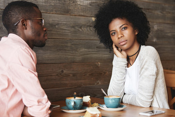 Two young black smart managers discussing very important question sitting at coffee shop, searching for new brilliant idea for developing strategy of successful business, woman having thoughtful look