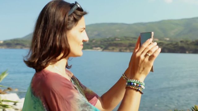 Woman recording beautiful view of the seaside on the smartphone
