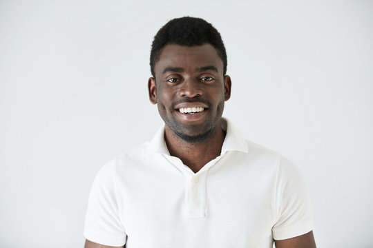 Cropped shot of smiling handsome young casually dressed African man model in white polo shirt, smiling showing his teeth, against studio background with copy space for your promotional information