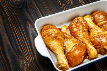 Raw chicken legs in baking dish on a wooden background