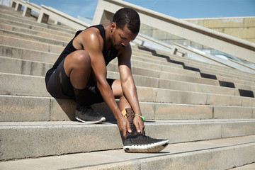 Muscular dark-skinned male athlete in black sportswear holding h