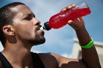 Tired and thirsty fit dark-skinned athlete in black tank top having break during intense outdoor...